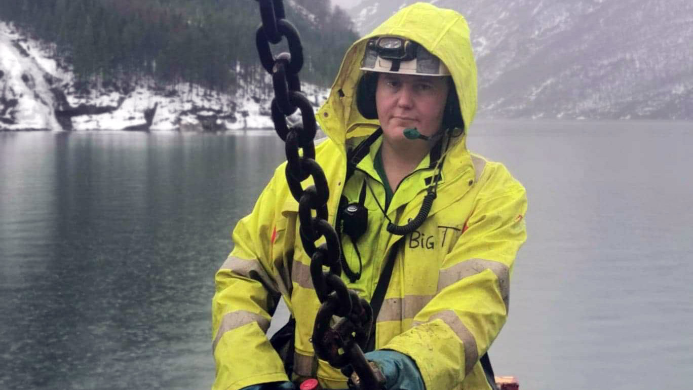 Mann i regntøy håndterer en stor kjetting. Foto.