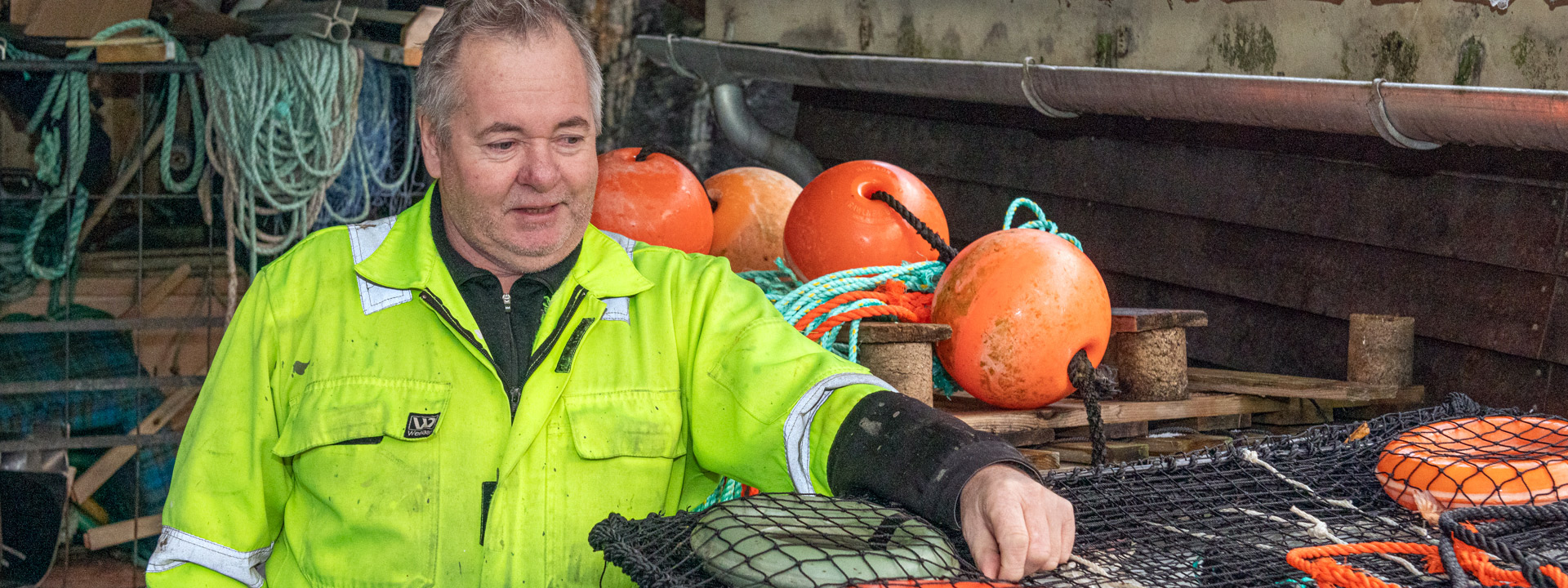 Mannlig ytrekfisker står ved siden av en stabel krepseteiner. Foto.