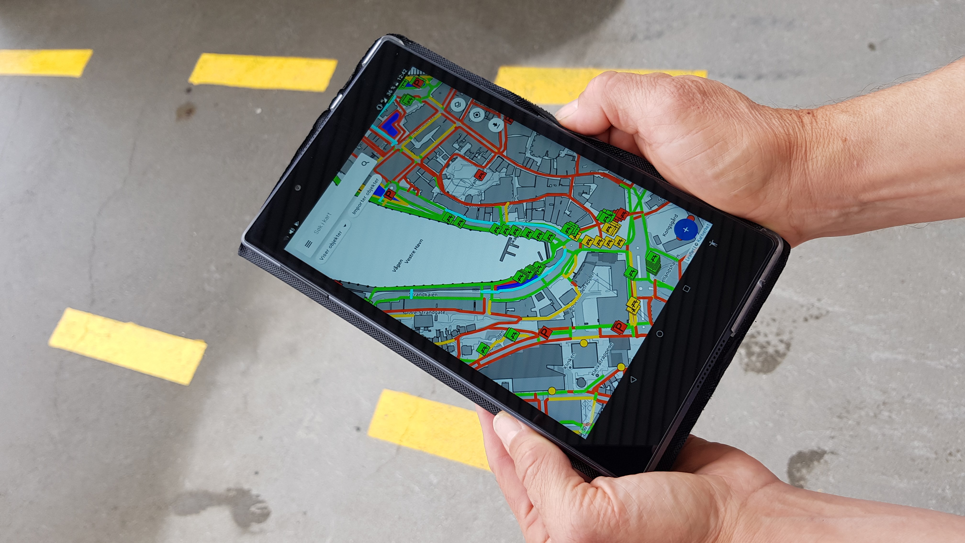 Hender holder et nettbrett hvor app'en for kartlegging av tilgjengelighet vises på skjermen